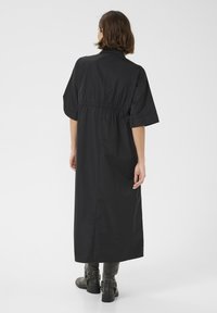 Abito nero lungo fino alla caviglia con una vestibilità rilassata, maniche corte e vita elastica. Texture liscia con un design semplice, senza motivi o dettagli.
