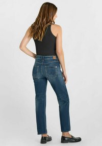 Jean en denim bleu avec une coupe droite, cinq poches et une taille mi-haute, accompagnés d'un débardeur noir et de mocassins noirs.