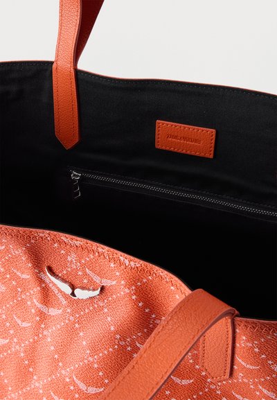 Sac cabas orange avec motifs étoiles et ailes, intérieur noir, poche zippée, et étiquette orange estampillée « ZADIG & VOLTAIRE » sur la doublure intérieure.