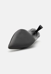 Black patent leather pointed-toe shoe with a smooth texture, sharp silhouette, and square heel. The sole is slightly curved and textured.