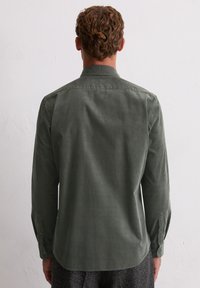 Chemise à manches longues vert olive foncé en tissu texturé, dotée d'un col classique et de poignets boutonnés, avec un ourlet courbé.