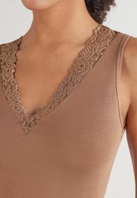 Top de tirantes marrón con un profundo escote en V adornado con intrincados detalles de encaje. La tela es suave y lisa, creando un look ajustado.