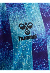 Blåt og lilla mønstret stof med Hummel-logoet i sort, med en plettet tekstur og vertikalt stribedesign.