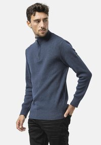 Pull à fermeture éclair quart en bleu marine avec une finition en tricot texturé, des poignets et un ourlet côtelés. Présente un logo sur la manche gauche.