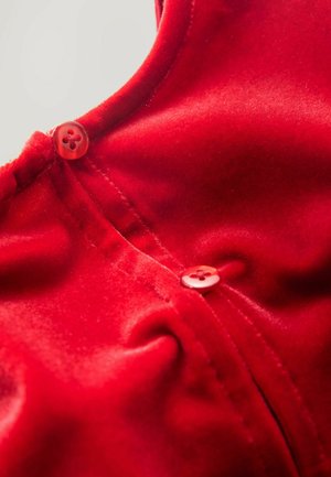 Abbigliamento in velluto rosso caratterizzato da una superficie liscia, chiusure con bottoni e arricciature vicino al collo. Design semplice con dettagli sottili.