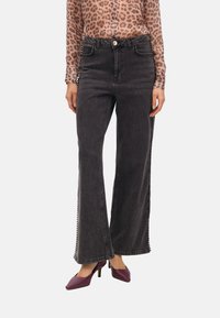 Svarta vida jeans med sidobroderier, en åtsittande midja och fransad fåll. Kombinerat med en leopardmönstrad topp och lila klackar.