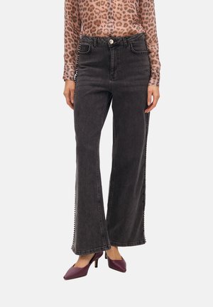 Black wide-leg jeans featuring side embellishments, a fitted waist, and frayed hem. Paired with a leopard print top and purple heels.