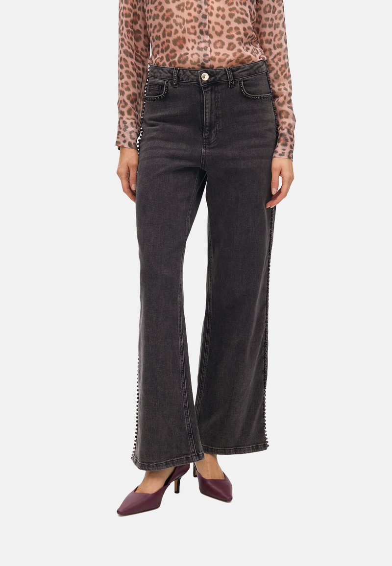 Svarta vida jeans med sidobroderier, en åtsittande midja och fransad fåll. Kombinerat med en leopardmönstrad topp och lila klackar.