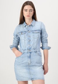 Svetlo modra denim obleka z oprijetim pasom, sprednjim gumbom, dvema žepoma na prsih in zvitimi rokavi. Gladka tekstura in klasična zasnova.