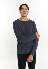 Maglione lungo navy a maniche lunghe con scollatura rotonda e polsini a costine, indossato sopra pantaloni neri, con una vestibilità rilassata.