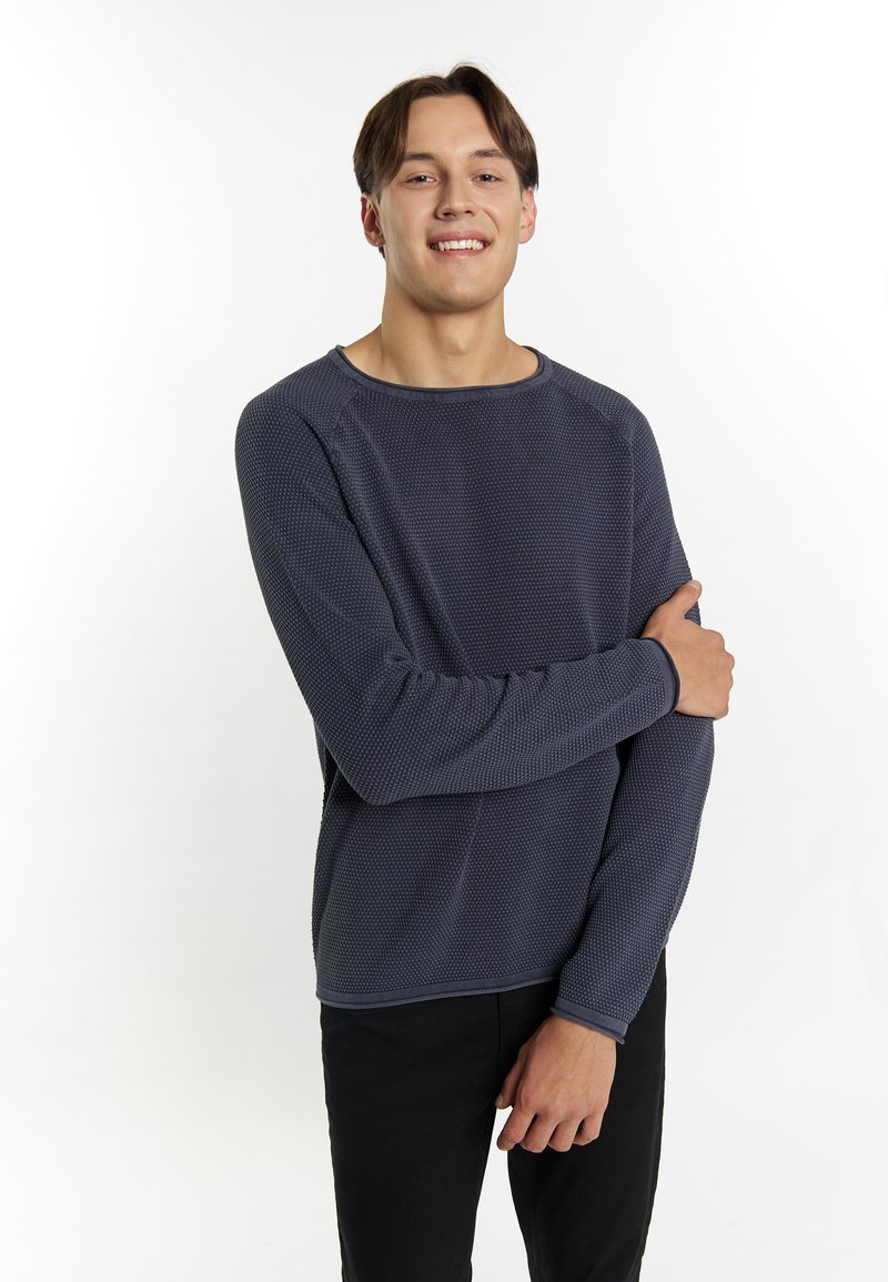 Maglione lungo navy a maniche lunghe con scollatura rotonda e polsini a costine, indossato sopra pantaloni neri, con una vestibilità rilassata.