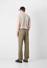 Beige polo shirt with short sleeves, khaki chinos, and black sneakers. The polo has contrasting cuffs; the chinos feature back pockets.