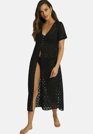 Robe de cover-up noire et transparente avec des manches courtes, en V et avec des boutons sur le devant ; présente un motif et une fente haute pour un détail supplémentaire.