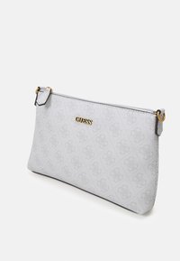 Pochette grise Guess avec motif de logo subtil, lettrage de marque doré et fermeture éclair supérieure inclinée sur fond blanc.