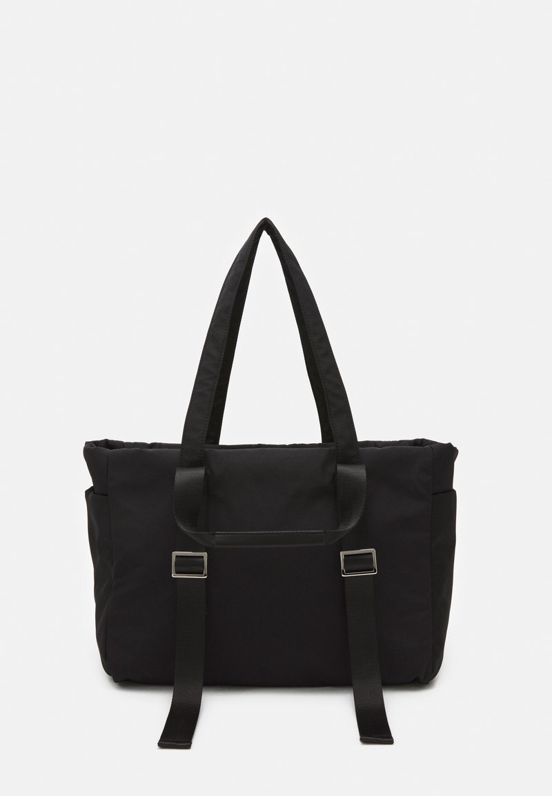 Sac fourre-tout rectangulaire noir avec deux poignées et des sangles avant réglables avec boucles argentées sur un fond uni.