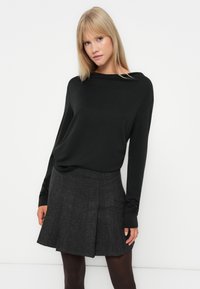 Haut noir à manches longues avec une coupe ample, associé à une jupe évasée à carreaux gris. Texture lisse avec un léger éclat.