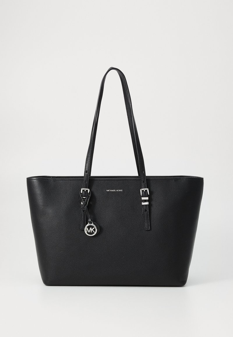 Black leather tote bag with textured surface, dual top handles, silver hardware, and an attached round MK logo charm.