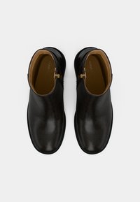 Botas de tornozelo pretas com um acabamento texturizado, couro liso e detalhes em zíper dourado, apresentando uma biqueira arredondada e um salto baixo.