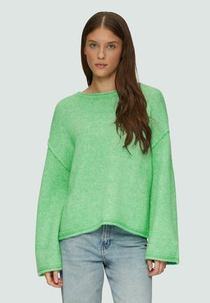 Grüner Strickpullover mit strukturierter Oberfläche, weiten Ärmeln und lockerem Schnitt, kombiniert mit hellblauen Jeans.
