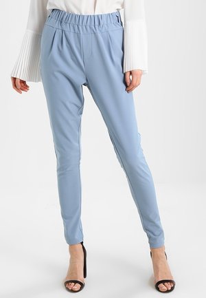 Pantalon extensible bleu clair avec une taille élastique. Design fuselé avec de subtils plis à l'avant. Assorti avec un haut blanc plissé.