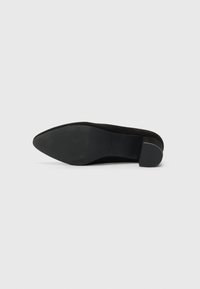 Black suede slip-on shoe with a rounded toe and a small block heel. The sole is textured, featuring horizontal ridges for grip.