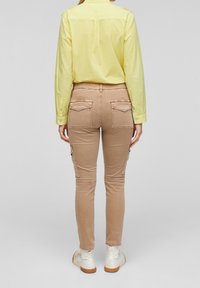 Camicia a maniche lunghe gialla chiara abbinata a pantaloni cargo beige con tasche posteriori e pattine laterali, indossata con scarpe bianche.