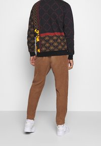 Sort mønstret sweatshirt med levende accenter og brune fløjlsbukser. Har forskellige motiver og en kontrastsyet kant, kombineret med hvide sneakers.