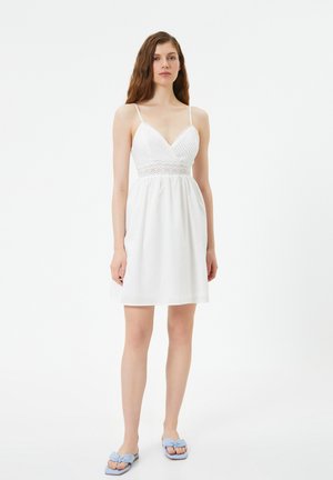 Abito bianco con corpino aderente caratterizzato da dettagli testurizzati, scollo a V profondo e spalline sottili; gonna svasata che arriva a metà coscia.
