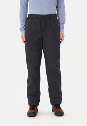 Schwarze wasserdichte Hosen mit einem elastischen Bund. Der Stoff ist glatt und bietet eine lockere Passform mit schmal zulaufenden Beinen. Getragen mit braunen Wanderschuhen.