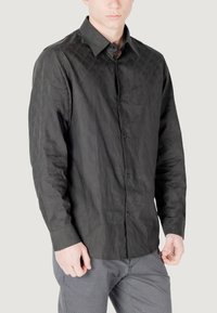 Camicia nera a maniche lunghe con bottoni, realizzata in un tessuto testurizzato con un sottile motivo geometrico; presenta un colletto a punta e polsini con bottoni.