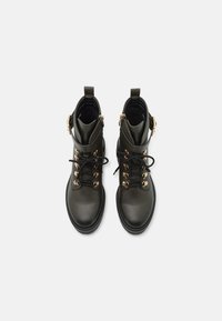 Botas de tobillo de cuero negro con ojales dorados y cordones negros. Punta redondeada, superficie texturizada y un acabo con hebilla lateral.