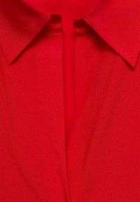 Gros plan sur un col de chemise rouge vif avec une patte de boutonnage cachée au centre.