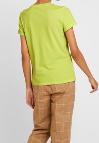 Limegrøn kortærmet t-shirt med rund hals, parret med brune ternede bukser med gule rutenet-mønstre. Glat tekstur.