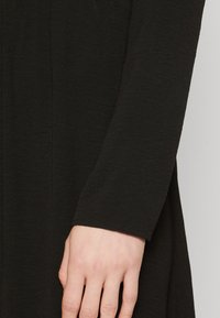 Μαύρο ρούχο με μακριά μανίκια και μαλακή, υφή. Το μανίκι έχει διακριτές ραφές και στρογγυλή μανσέτα.