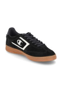 Adidași negri din suede cu talpă din cauciuc bej, prezentând un logo alb pe lateral și șireturi închise la culoare. Design cu profil jos și linii elegante.