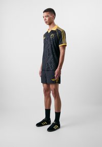 Maillot de sport noir avec col et accents jaunes, présentant un motif. Assorti à un short noir et des chaussures noires avec des rayures jaunes.
