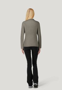Rippierter, olivgrüner Pullover mit langen Ärmeln und tailliertem Schnitt, kombiniert mit schwarzen Schlagjeans und Sportschuhen. Rückansicht gezeigt.
