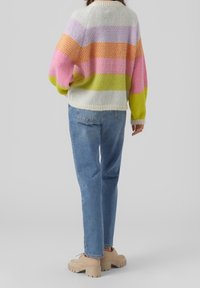 Pull en maille à rayures multicolores rose, orange, jaune et vert. Présente une coupe décontractée et un col côtelé. Associé à un jean bleu clair.