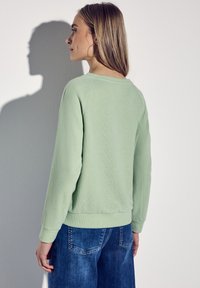 Ljusgrön sweatshirt med ribbad struktur, rund halsringning och långa ärmar. I kombination med blå denimjeans som har bakfickor.