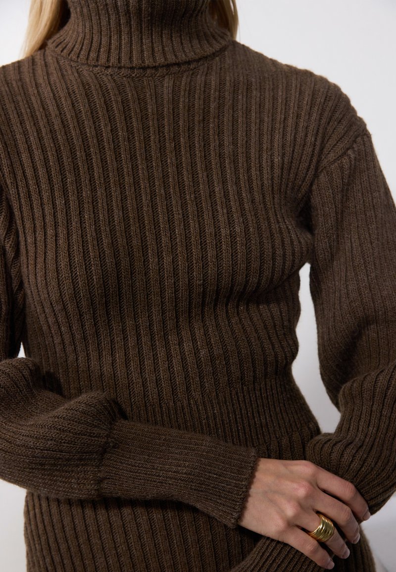 Pull en maille côtelée marron, doté d'une texture douce, d'une coupe ajustée et de manches longues avec des poignets retournés. Chaleur et confort remarquables.