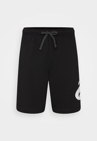 Shorts de sport noirs en tissu doux, dotés d'une taille élastique avec cordon de serrage et d'un grand logo blanc sur la cuisse gauche. Texture lisse, arrivant au genou.