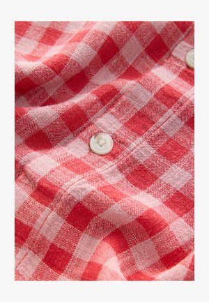 Tissu de chemise à carreaux rouge et rose avec une texture douce, ornée d'un bouton rond blanc. Motif à carreaux bien en évidence sur l'ensemble du matériau.