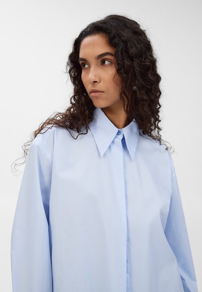 Camicia azzurra chiara a maniche lunghe con colletto classico, chiusura con bottoni e tessuto liscio. Presenta una vestibilità rilassata e un design minimalista.