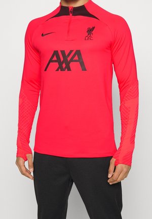 Mann trägt ein rotes Liverpool FC Trainingsoberteil mit schwarzem AXA Sponsorlogo und Nike-Swoosh, kombiniert mit schwarzen Hosen.