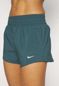 Pantalones cortos deportivos de Nike en color azul verdoso, con una cinturilla elástica fruncida y un logo blanco. Fabricados con un material ligero y transpirable de textura suave.