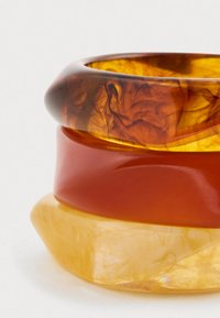 Sett med tre armbånd i gjennomsiktig rav, oransje og gule materialer; glatte overflater med buede kanter og varierende bredder.