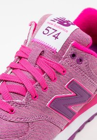 Närbild av rosa New Balance 574-sneakers med rosa snören och lila "N"-logotyp på den texturerade tygöverdelen.