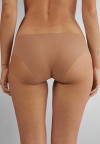 Naadloze, huidskleurige bikini slipjes van zacht, glad materiaal met minimale bedekking en zonder zichtbare randen voor een discrete pasvorm.
