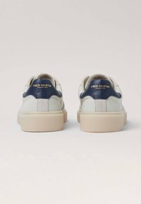 Zapatillas blancas de cuero con acentos en azul marino. Suela gruesa de color crema y detalles de ante. Logotipo dorado visible en el talón, diseño minimalista.