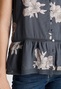 Dark gray peplum top with light floral pattern, round neckline, button closure, and lace trim at hem. Soft fabric with smooth texture.